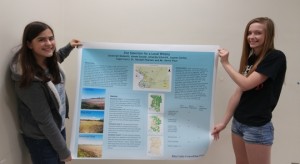 Edwardsville High School students Lauren Serfas (left) and Amanda Schmidt display their poster their group project in their AP Geography course. The course is augmented by SIUE professor Randall Pearson and six SIUE students. (Photo by Joseph Lacdan)